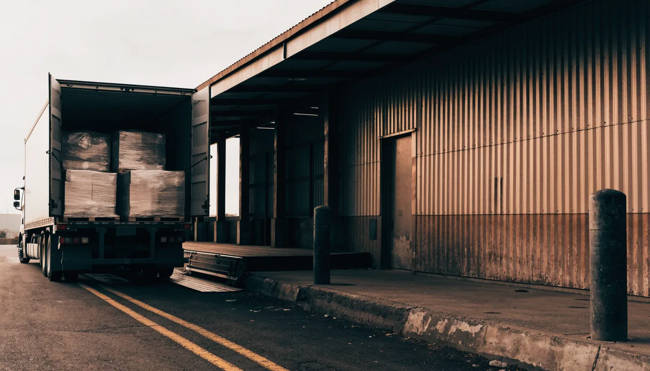 A freight truck backed into a warehouse loading dock with pallets inside