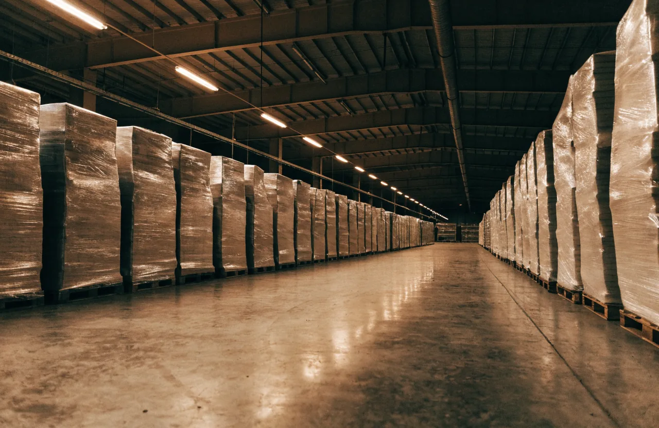 Long rows of wrapped pallets staged under warehouse lights